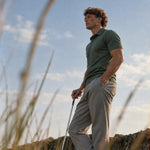 Full-length side view of the Deep Cypress Biome polo worn with gray trousers and a golf club.