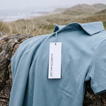 Light blue Glacier Biome polo laid on a stone wall with a Hampton & Lake hangtag.