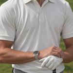 Front view of the off-white Limestone Biome golf polo worn by a golfer holding a club.