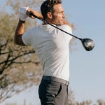 Golfer completing a driver swing in the Limestone Biome polo and dark trousers.