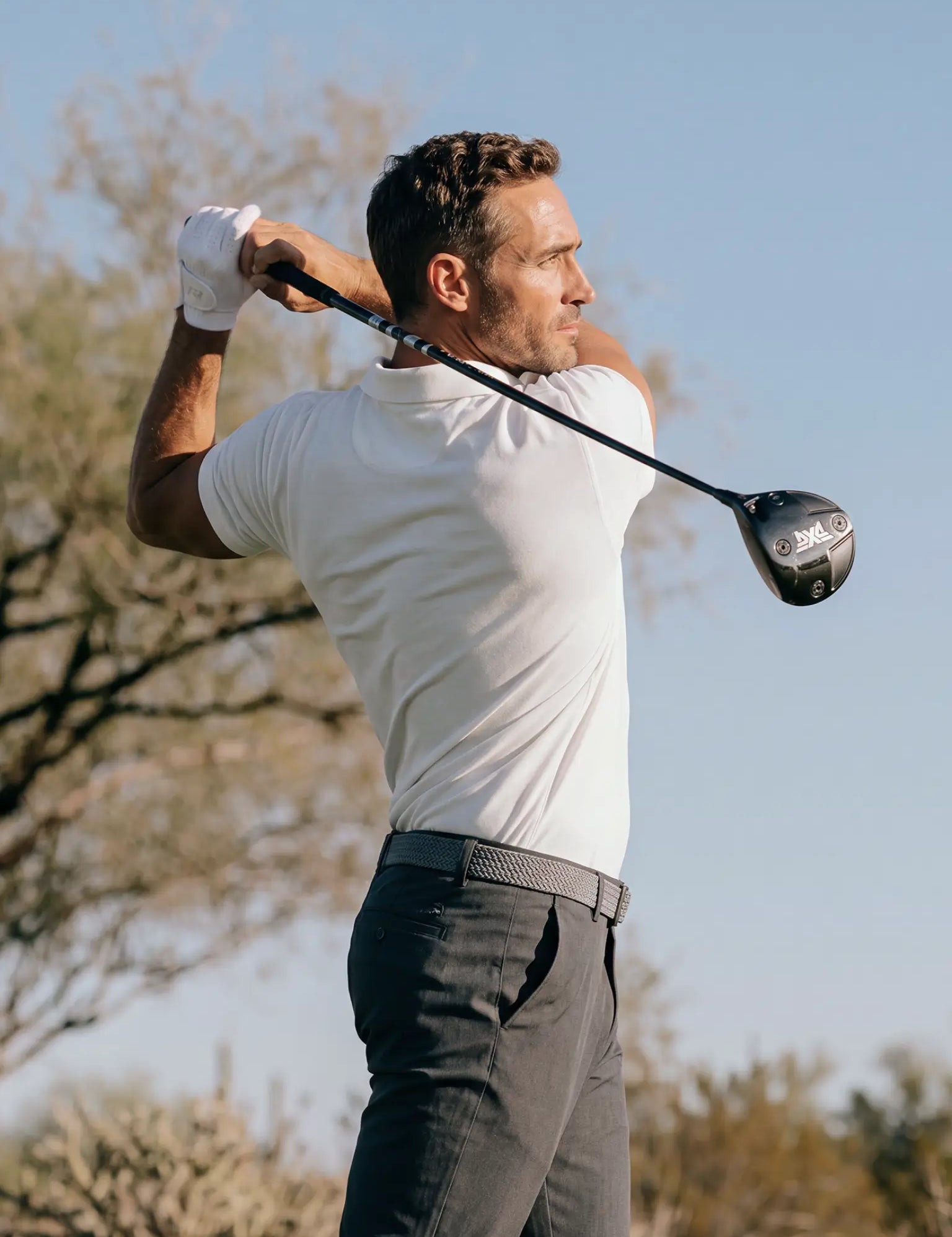 Golfer completing a driver swing in the Limestone Biome polo and dark trousers.