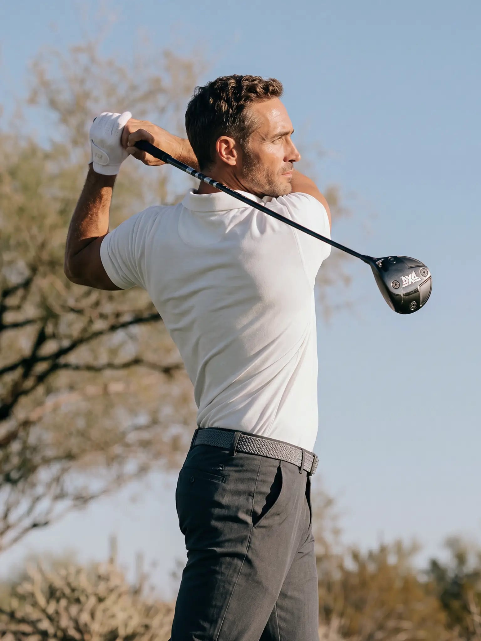 Golfer completing a driver swing in the Limestone Biome polo and dark trousers.