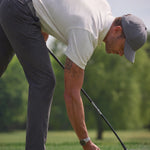 Golfer wearing the Limestone Biome polo bending down to place a ball on a tee.