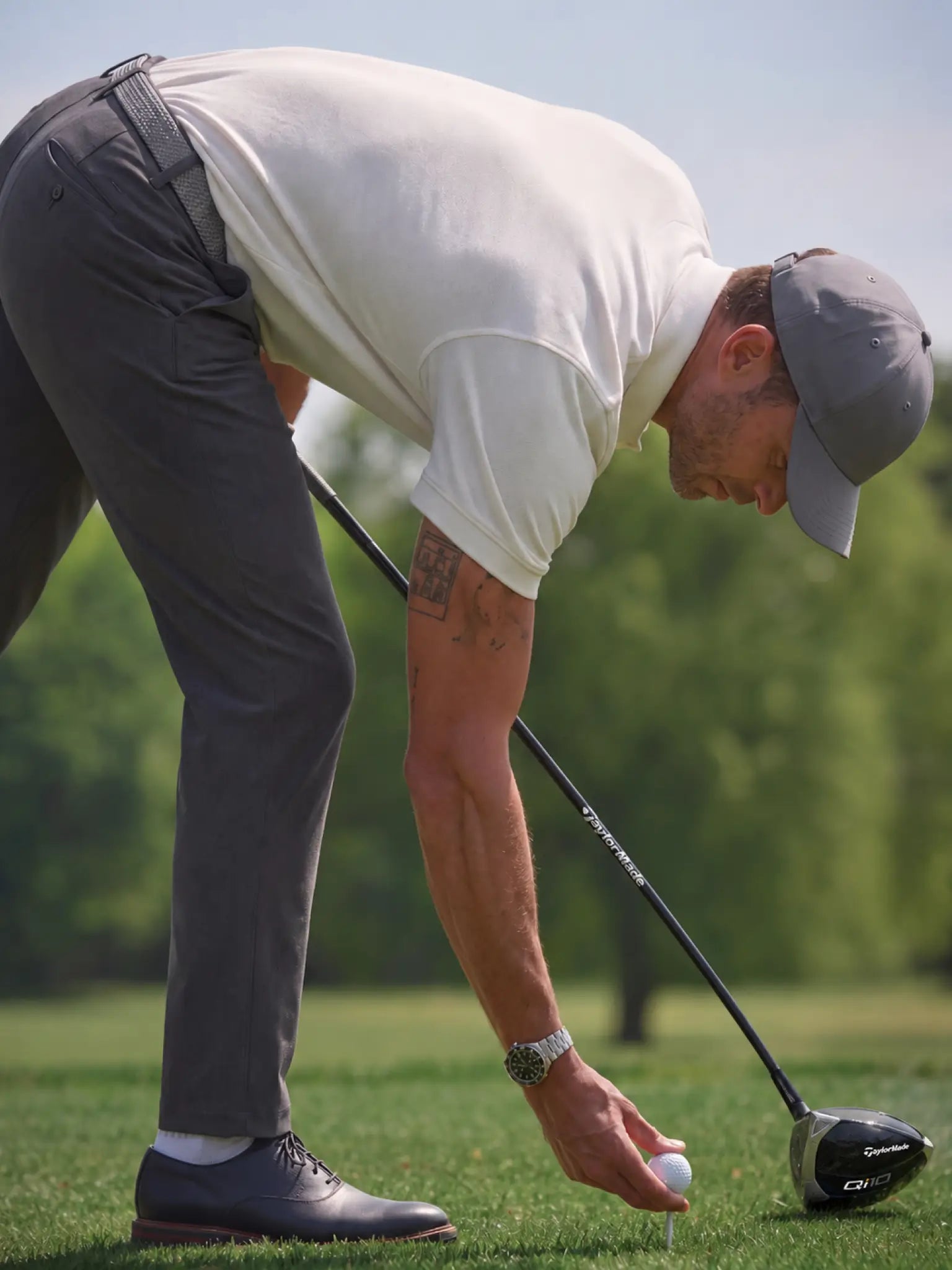 Golfer wearing the Limestone Biome polo bending down to place a ball on a tee.