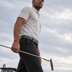 Low-angle view of a golfer carrying a putter while wearing the Limestone Biome polo.