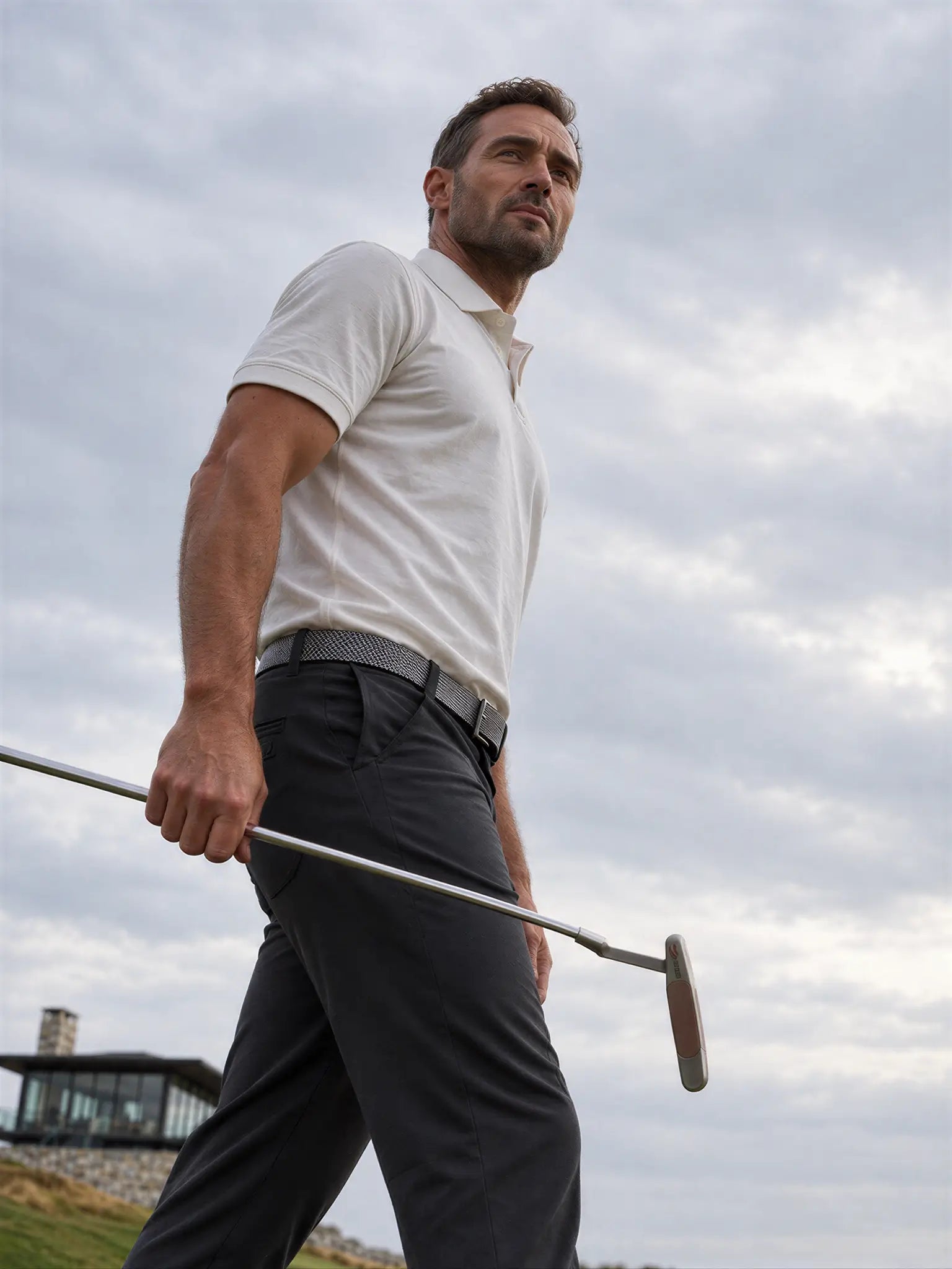 Low-angle view of a golfer carrying a putter while wearing the Limestone Biome polo.