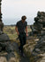 Model wearing the charcoal Volcanic Ash Biome golf polo while walking between coastal rocks with a golf club.