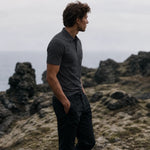 Side view of the Volcanic Ash Biome polo worn with black trousers beside a rocky coastline.