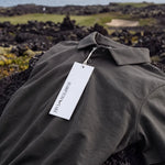 Charcoal Biome polo laid across coastal rocks with a Hampton & Lake hangtag.