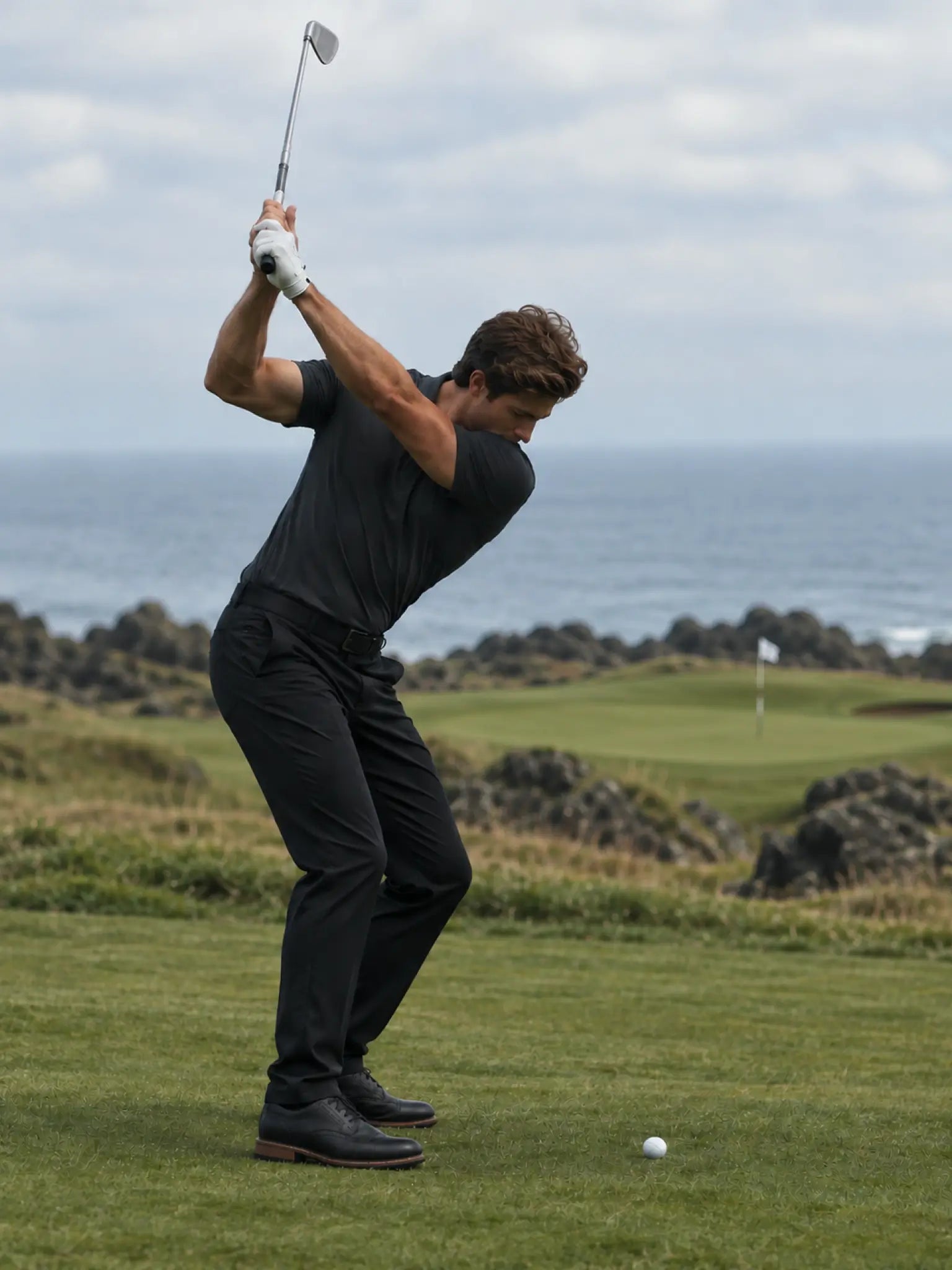 Golfer at the top of a backswing wearing the Volcanic Ash Biome polo.